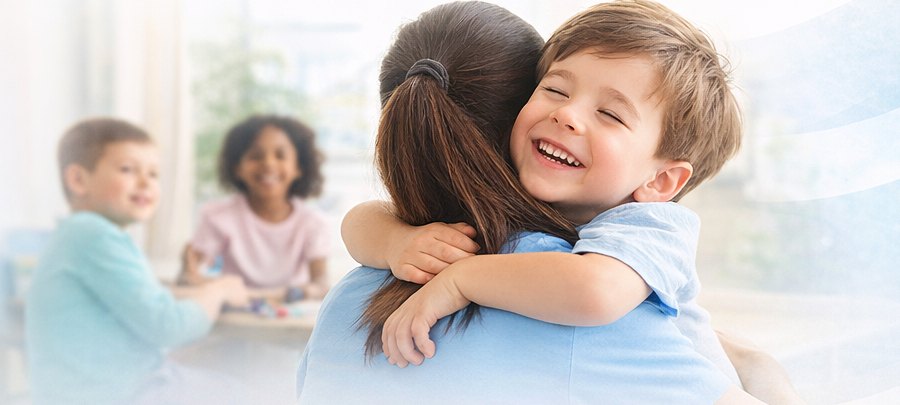 Un bambino sorride abbracciando una terapista, sullo sfondo altri bambini giocano